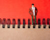 Small male figurine standing with hands in pockets on a spiral-bound notebook against a bright red background.