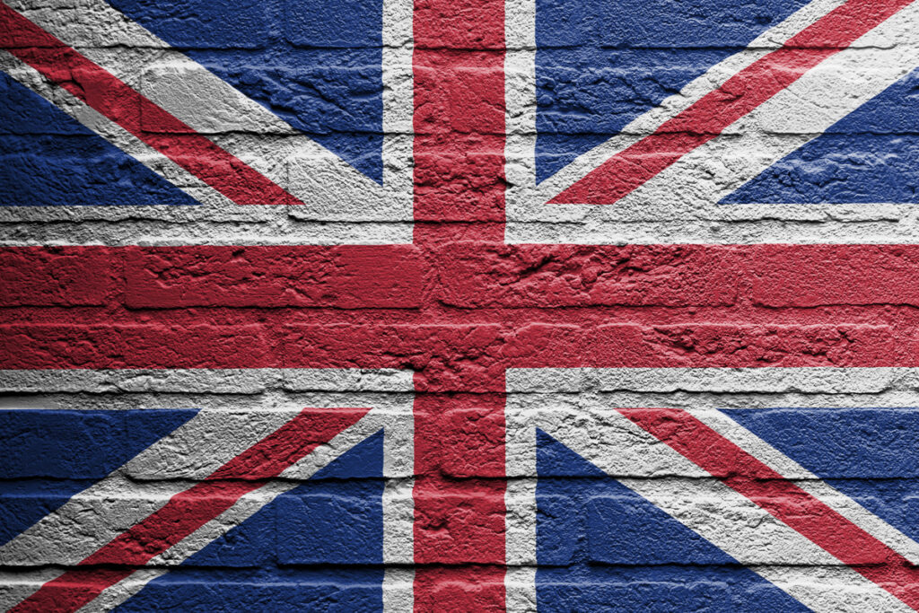Union Jack flag painted on a rough brick wall surface.