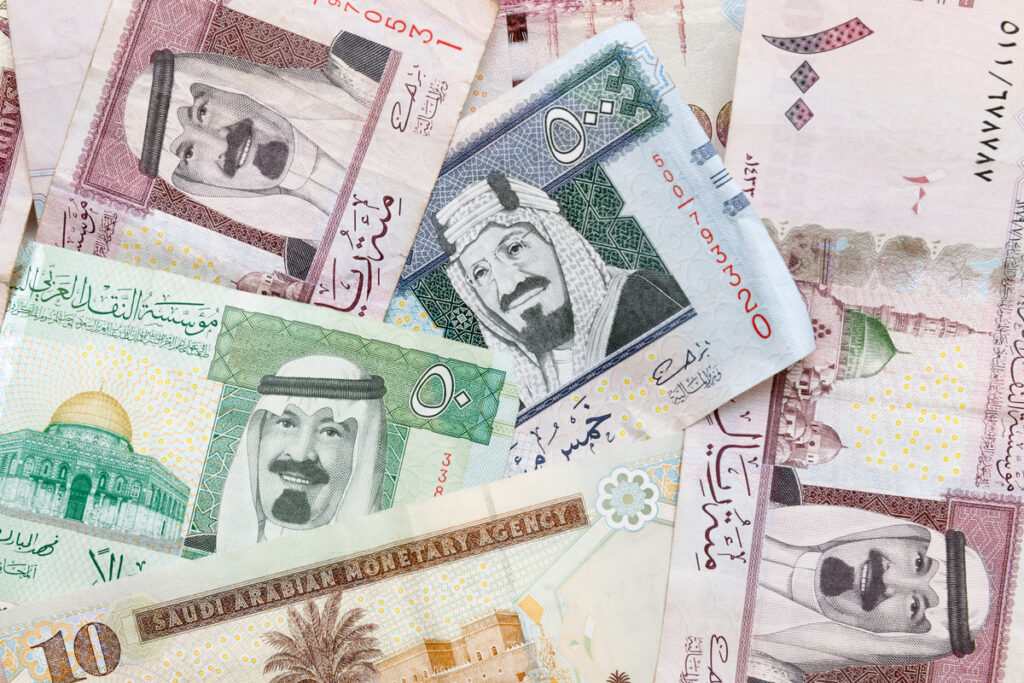 Collage of colorful Saudi Arabian riyal banknotes overlapping, showing portraits and denominations.