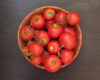 Basket of ripe red tomatoes with green stems on a dark wooden surface beneath.