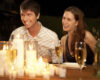 Smiling couple seated at a candlelit dinner table with wine glasses nearby.