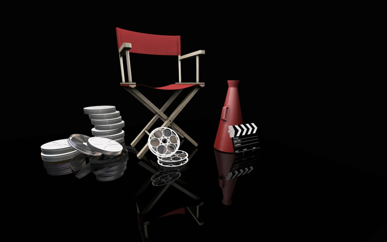 Film production gear: red director's chair, stacked movie reels, a clapperboard, and a red studio light on a reflective black surface.