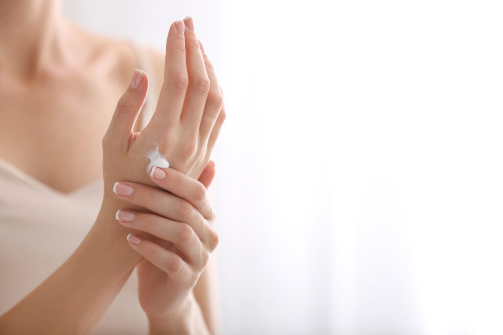 Close-up of hands with a small amount of white cream on the wrist, applying skincare moisturizer