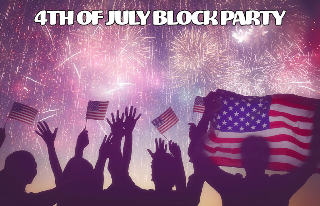 Crowd cheering with American flags as fireworks light the sky at a 4th of July block party.