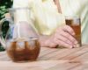 Person in a pale yellow shirt sits at a wooden outdoor table with a pitcher and a glass of iced tea nearby on the table.