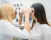 Optometrist uses a phoropter to inspect the patient's eyes during an eye exam in a clinic setting.