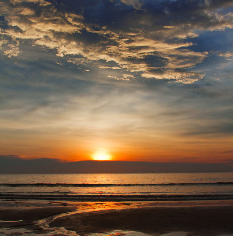 Sunset over the ocean with orange horizon, golden clouds, and reflections on wet sandy shore.