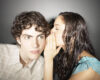 Woman whispering a secret into a young man's ear as he looks ahead