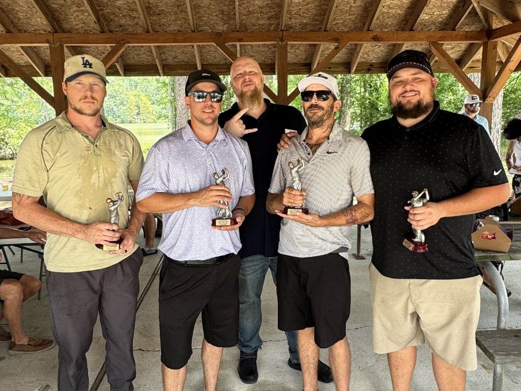 Five men stand under a wooden pavilion, each holding a small trophy from a tournament award ceremony.