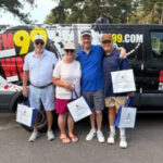 Four adults pose in front of a branded van, each holding a white tote bag.