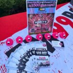 Promotional display with pink pig toys, flyers, and a sign advertising a $500 gas card drawing for Pinky’s Junk Removal truck promotion on a table outdoors.
