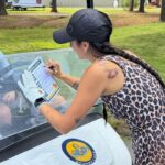 Woman in a leopard-print dress signs a form on a golf-cart at Stumpy Lake Golf Course.