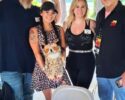 Four adults posing under a wooden pavilion; a woman in a leopard-print dress holds a plush owl with others smiling nearby.