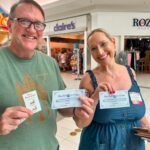 Smiling man and woman in a mall holding Blue Bell Ice Cream vouchers and a guest card.