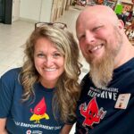 Two adults smiling for a selfie in a mall, wearing blue “I Am Empowerment Day” shirts for the American Red Cross event and mascot graphics.