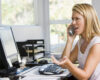 Woman at a cluttered office desk, talking on a corded phone and gesturing with her other hand.