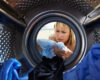 Woman inspecting a blue shirt inside a front-loading washing machine drum, looking concerned or focused.