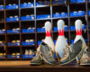 Three bowling pins with red stripes stand between two pairs of gray bowling shoes on a wooden lane.
