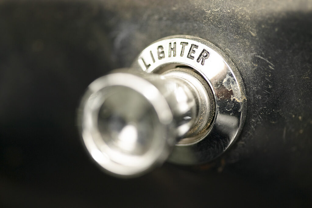 Close-up of a chrome lighter ignition knob labeled 'LIGHTER' on a dark, worn surface.