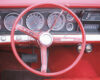Red vintage car interior with a large circular steering wheel and classic gauge cluster on the dashboard