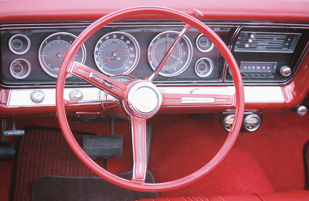Red vintage car interior with a large circular steering wheel and classic gauge cluster on the dashboard