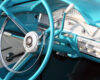 Turquoise vintage car interior with a large chrome steering wheel and classic dashboard gauges.
