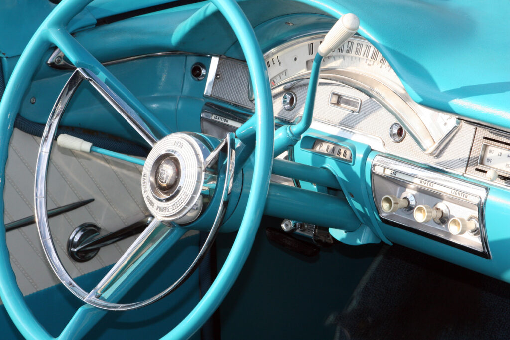 Turquoise vintage car interior with a large chrome steering wheel and classic dashboard gauges.