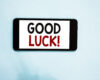 Smartphone displaying the words 'GOOD LUCK!' on a white screen against a light blue background.