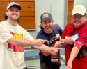 Three men in a hallway smiling and pointing at each other toward the camera.