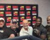 Five men pose for a photo in a radio studio in front of a 'Rumble in the Morning' banner.