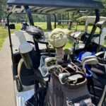 Golf bag with clubs in a cart, topped by a Yoda plush toy peeking over the irons on a sunny golf course.