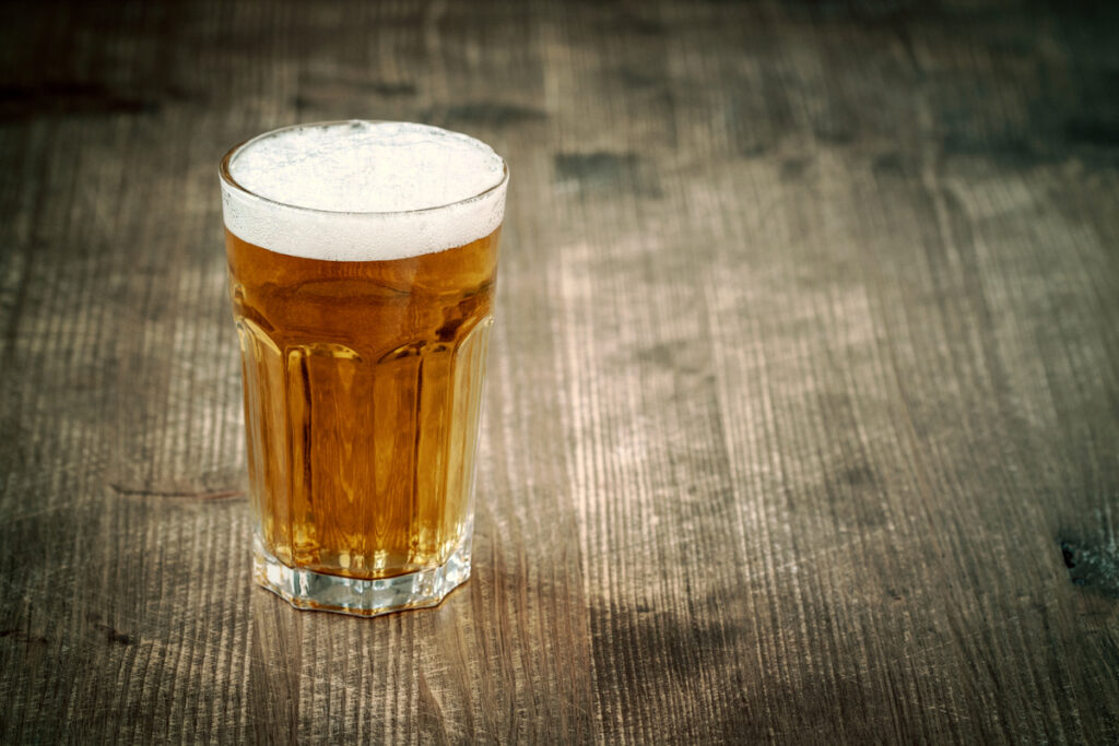 Amber beer in a frothy pint glass on a weathered wooden table