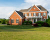 Brick two-story house with white shutters and manicured front yard on a sunny day.