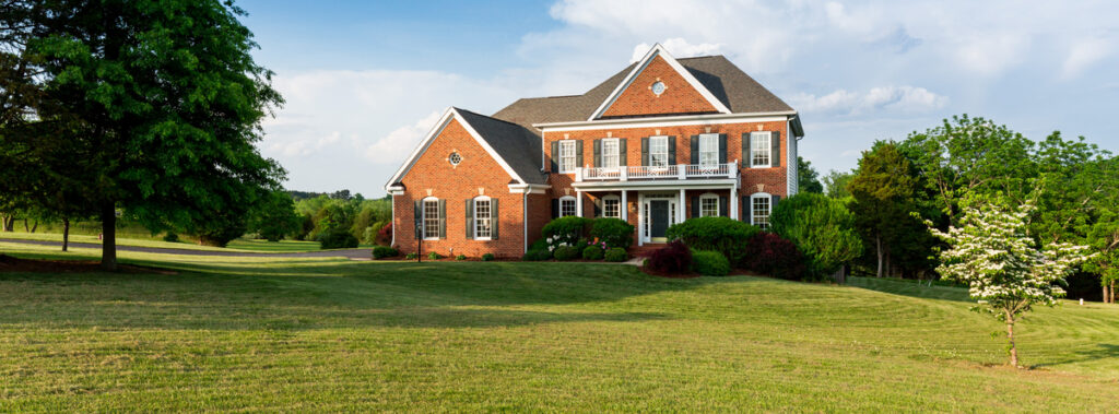 Brick two-story house with white shutters and manicured front yard on a sunny day.