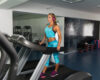 Woman in a bright blue workout outfit walks on a treadmill wearing pink headphones in a gym.